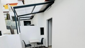 A narrow outdoor patio with a tiled floor, a white table with two chairs, and a metal railing.