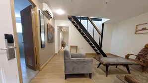 Een ruime woonkamer met een grijze fauteuil, een houten salontafel en een trap naar een verdieping boven.