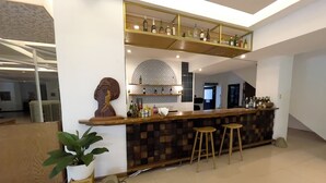 Een moderne bar met een geruit houten aanrecht, krukken en een diverse collectie flessen op planken.