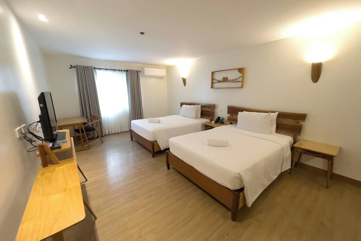 A hotel room with two beds, a desk, a chair, a television, and a window with curtains.