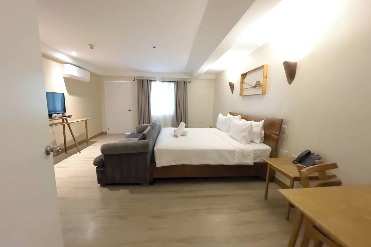 A hotel room with a bed, a desk, a chair, a TV, and a window with curtains.