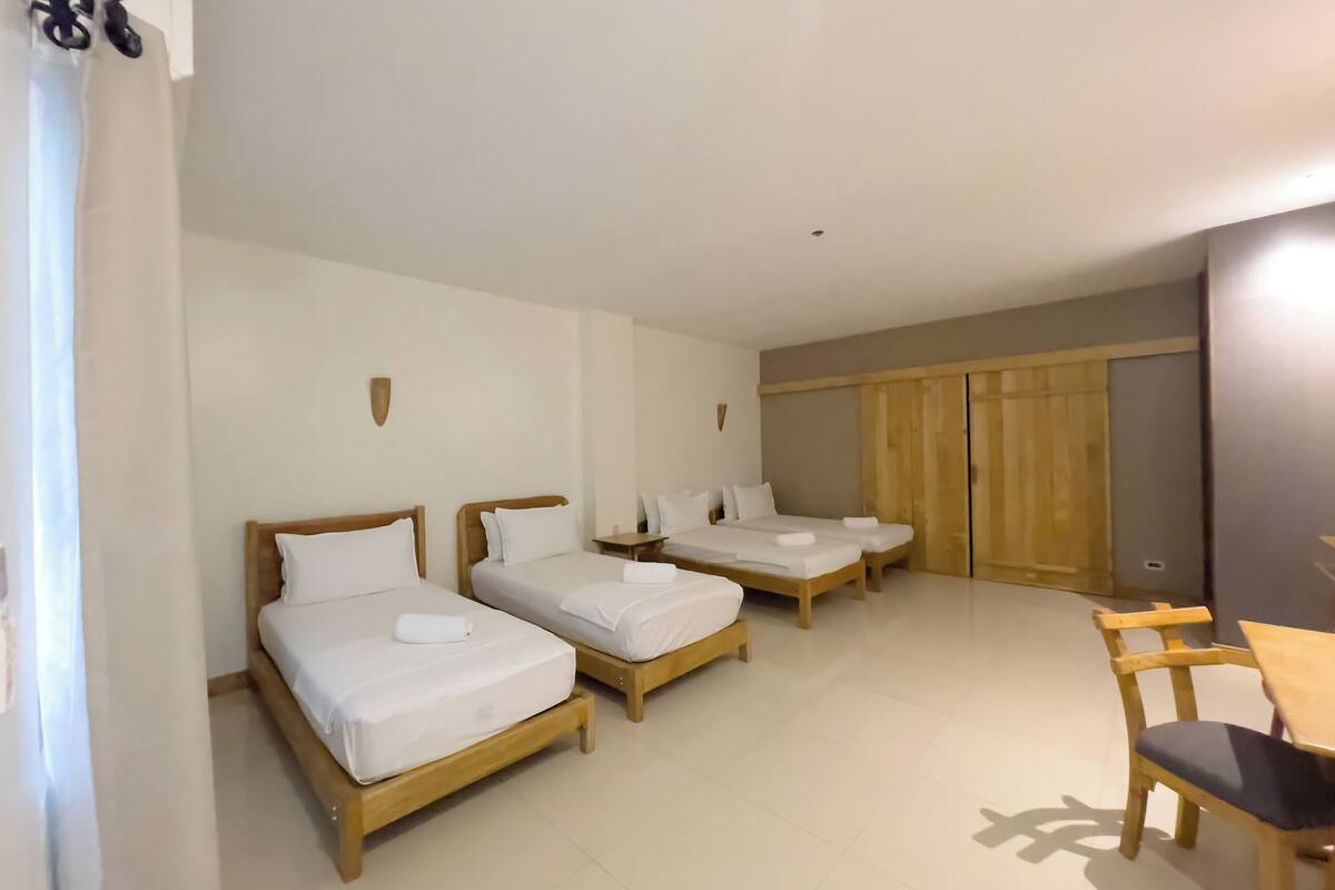A hotel room with three wooden beds, a wooden desk, and a chair.