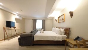 Een hotelkamer met een bed, een bureau, een stoel, een televisie en een raam met gordijnen.