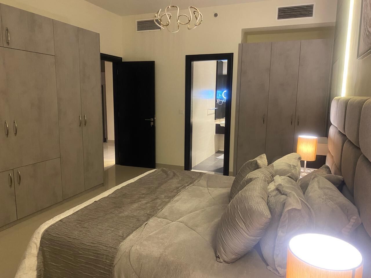 A bedroom with a large bed, grey wardrobe, and a bedside lamp.