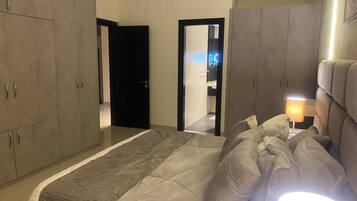 A bedroom with a large bed, grey wardrobe, and a bedside lamp.