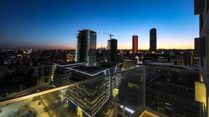 A cityscape at dusk with high-rise buildings, including a construction crane, and a brightly lit building with a visible sign.
