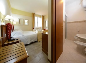 A hotel room with a bed, bedside table, lamp, and a view of the bathroom.
