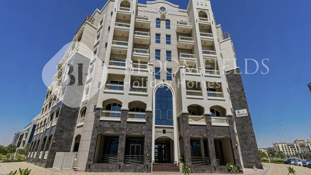Een meerlaags hotel met een centrale ingang, balkons en een betegelde binnenplaats.