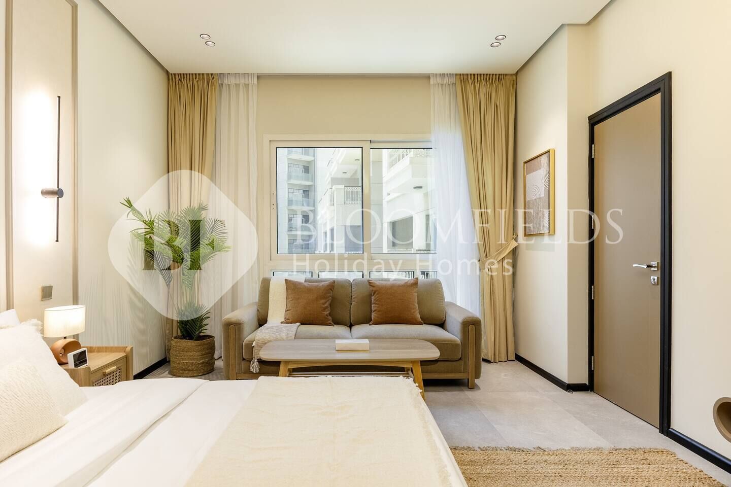 A modern hotel room with a bed, a sofa, a small table, and a potted plant.