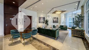 A spacious hotel lobby with a modern design, featuring a green sofa, a dining area with a glass table and chairs, and a large window offering a view of the outside. - Bloomfields Stylish Stu Burj View Arjan  (Dubai)