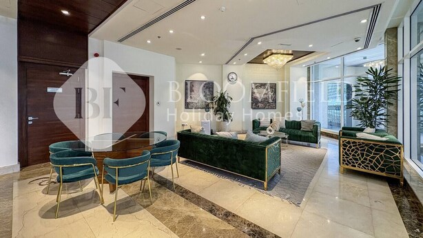 Eine geräumige Hotelhalle im modernen Stil, mit einem grünen Sofa, einem Essbereich mit Glastisch und Stühlen sowie einem großen Fenster mit Blick nach außen.