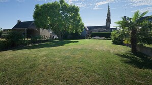 A grassy courtyard with a large tree, a stone building, and a tower in the background. - Rental for 2 people, 7 km from Louvigné-du-Désert (35420) (Monthault)