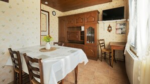A dining area with a table set for two, wooden chairs, a cabinet with glass doors, a television mounted on the wall, and a window with curtains. - Rental for 2 people, 7 km from Louvigné-du-Désert (35420) (Monthault)