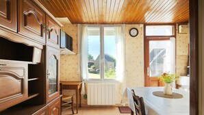 A kitchen with wooden cabinets, a dining table with a vase of flowers, and a view through a window. - Rental for 2 people, 7 km from Louvigné-du-Désert (35420) (Monthault)