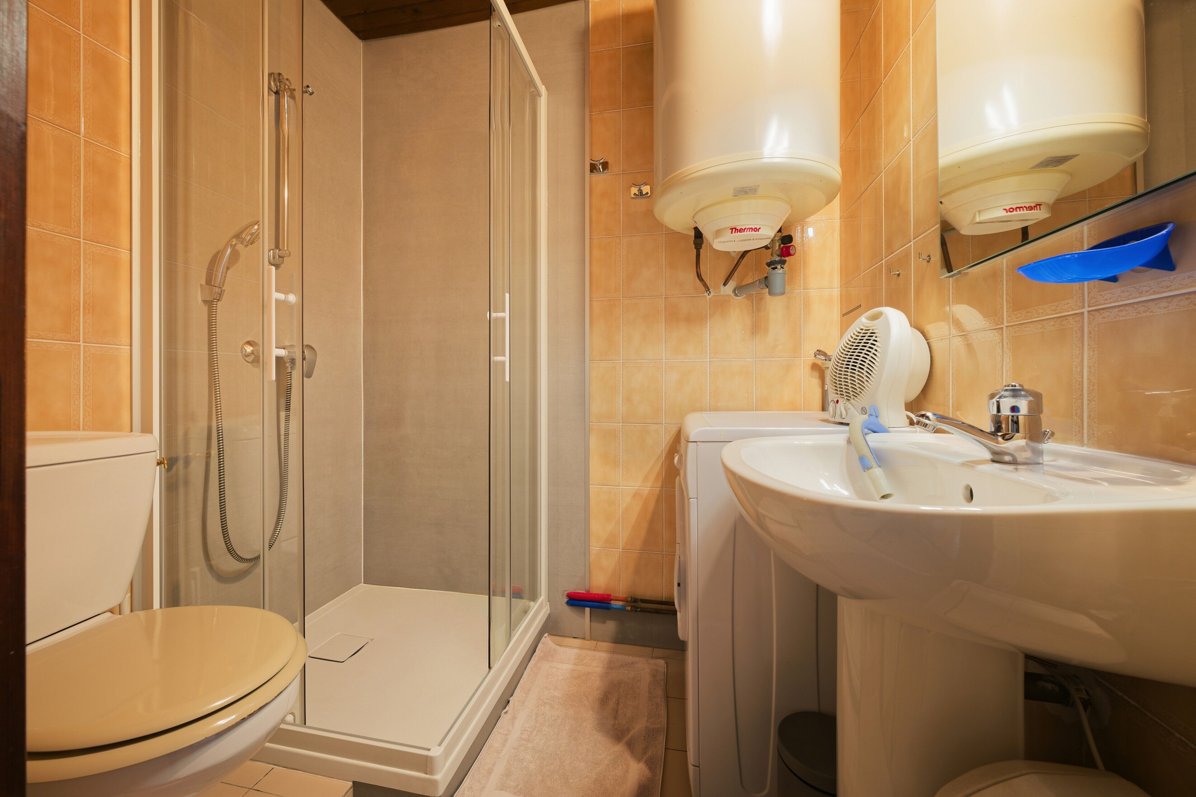 A bathroom with a toilet, a shower enclosure, a sink, and two wall-mounted heaters.