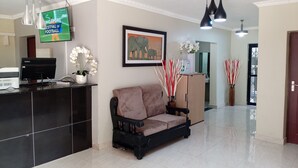 A reception area with a black desk, a brown sofa, a framed elephant painting, and a TV displaying the Singapore Festival of Football. - K-View Boutique Hotel (Mzuzu)