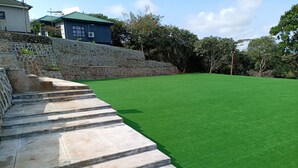 A set of stone steps leading to a green lawn area with a stone wall and a building with a green roof in the background. - K-View Boutique Hotel (Mzuzu)