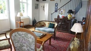 A living room with a sofa, armchair, and a wooden coffee table. There is a staircase with a railing, a lamp, and a radiator.