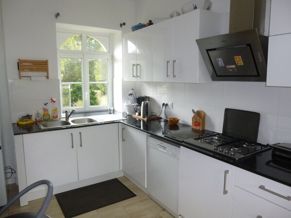A modern kitchen with white cabinets, a black countertop, a dishwasher, and a window providing natural light. - Charming family home (Melgven)