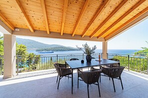Un espacio de comedor al aire libre cubierto, con una mesa y sillas, con vistas panorámicas a un lago y montañas.
