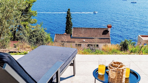 Una terraza con una silla de descanso, una mesa con bebidas y vista al mar con barcos.