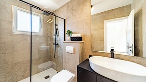 Un baño moderno con ducha de vidrio, inodoro blanco, lavamanos grande y espejo.