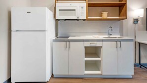 A compact kitchen with a white refrigerator, a microwave, and a sink with a faucet.