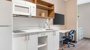Een moderne keuken met witte kasten, een ingebouwde magnetron en een houten plank.