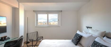 A modern hotel room with a large bed, a desk with a computer, a chair, and a window with a city view.