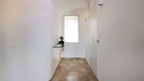 A narrow hallway with a marble floor, a small plant on a marble ledge, and a window at the end. - Ruggero City View apartment by Wonderful Italy (Palermo)