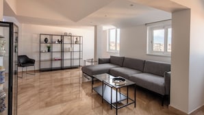 A modern living room with a sectional sofa, a glass coffee table, a black chair, and a black shelving unit with decorative items. - Ruggero City View apartment by Wonderful Italy (Palermo)