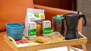 Una bandeja de madera con una cafetera, un recipiente azul y alimentos sobre una mesa.