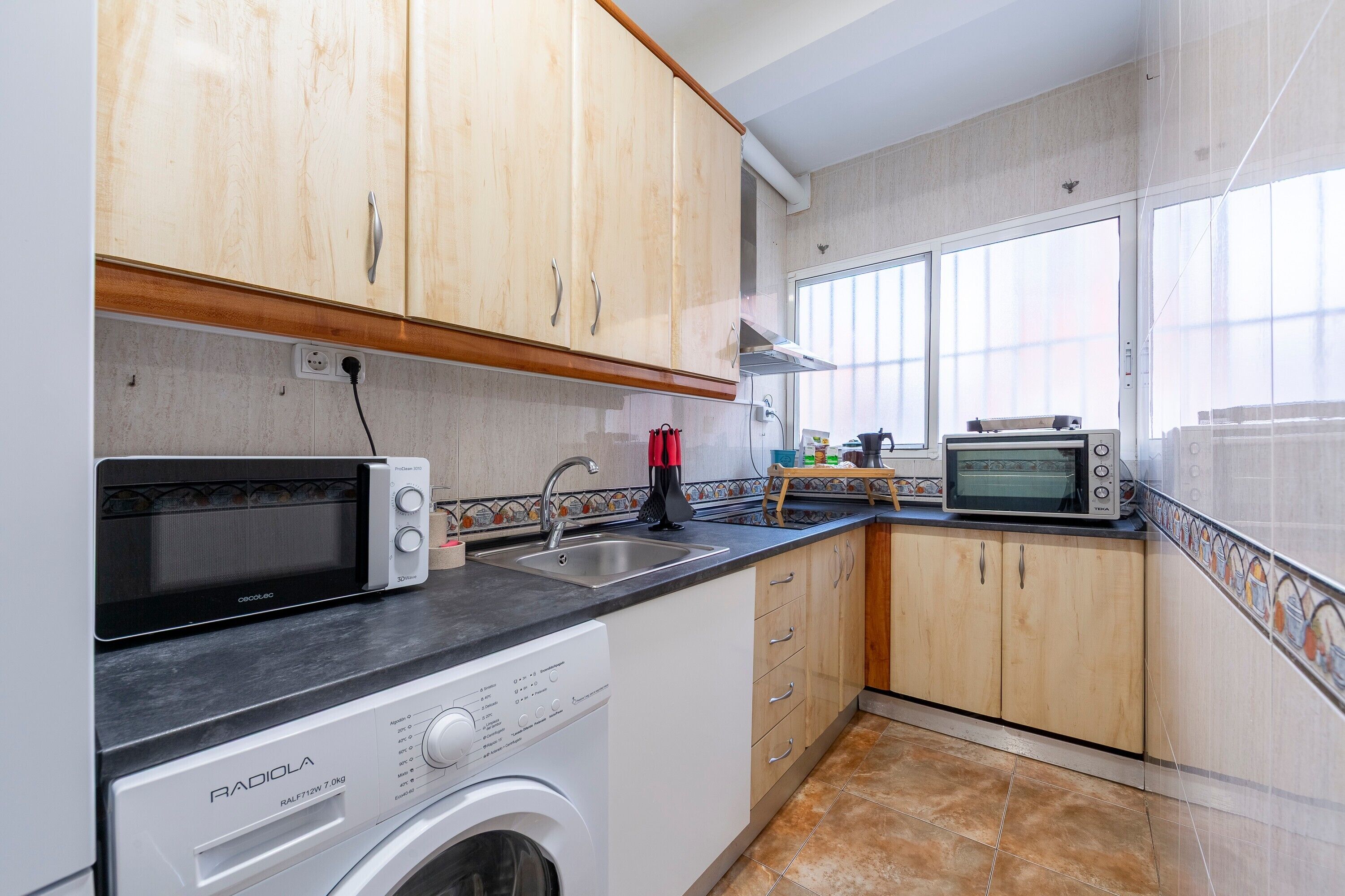 A kitchen with a washing machine, a microwave, a toaster, and a sink.