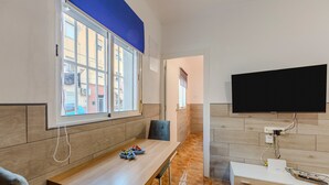 Una habitación moderna con una mesa de comedor de madera, un televisor montado en la pared y un ventanal con toldo azul.