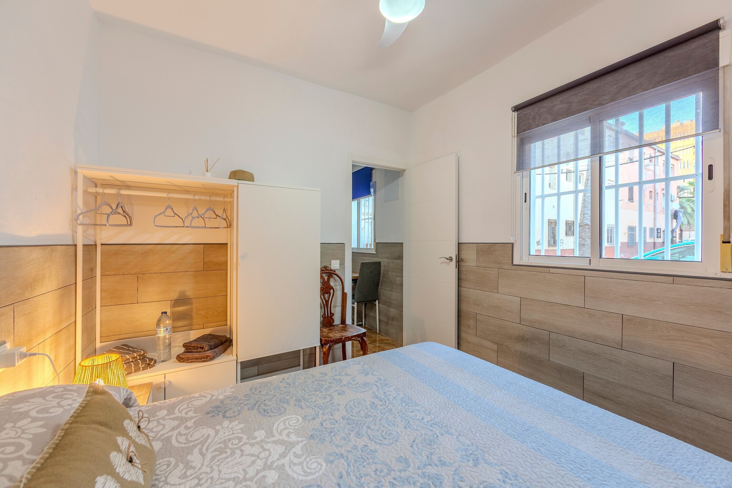 A bedroom with a bed, a wooden wardrobe, a desk, and a window with a view.