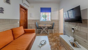 Un espacio habitable compacto con sofá, una mesita, televisor montado en la pared y ventana con persiana azul.
