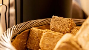 Ein Korb gefüllt mit Lebensmitteln, möglicherweise Brot oder ähnlichen Produkten, vor dunklem Hintergrund und mit metallischen Elementen.