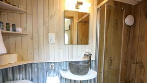Ein Badezimmer mit Holzwandverkleidung, einem Steintonne, einem Spiegel und einer Duschkabine.