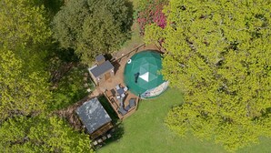 Eine Luftaufnahme einer Anlage mit Swimmingpool, einer Terrassenfläche mit Gartenmöbeln und einem kleinen Gebäude mit Satteldach.
