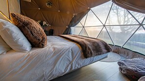Ein gemütliches Zelt-Schlafzimmer mit Bett, Kissen und Blick durch das Fenster.