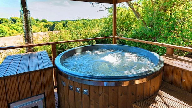 Un bain à remous installé sous une pergola en bois, offrant une vue sur un paysage verdoyant et luxuriant.