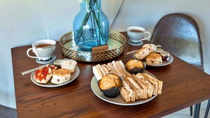Une table avec un vase bleu rempli de fleurs, deux tasses de café et une variété de viennoiseries et de sandwichs.