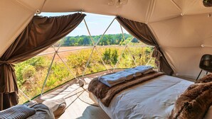 Une pièce confortable aménagée sous une tente, avec un lit, une chaise et une vue sur la campagne.