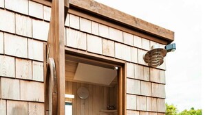 Une cabane en bois dotée d’une terrasse en bois, de toilettes et d’une petite étagère contenant des articles de toilette.
