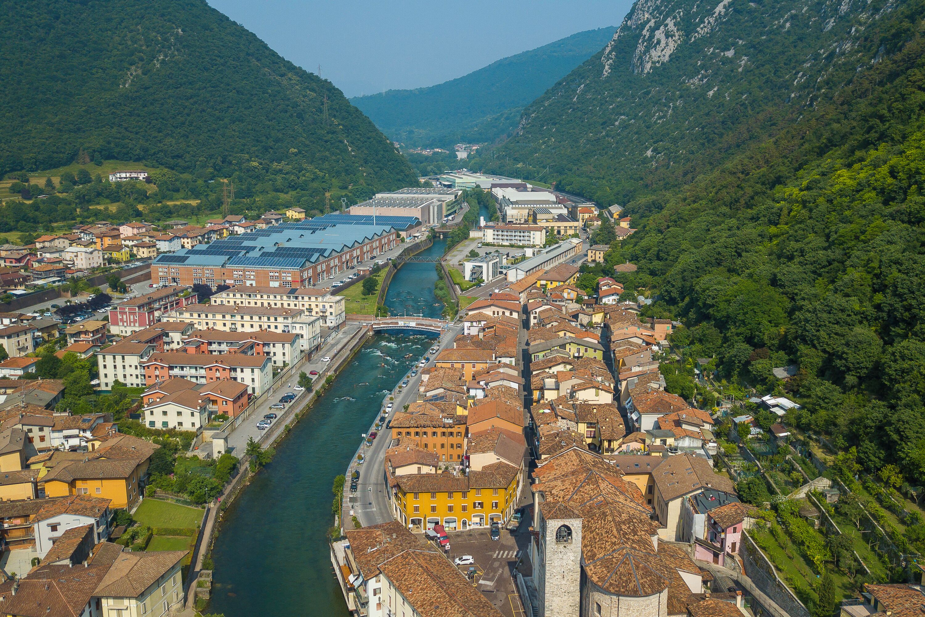 Une rivière traverse une ville, avec des bâtiments de chaque côté, un pont et des montagnes en arrière-plan.