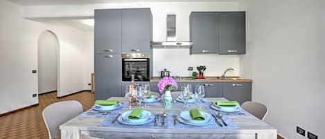 A modern kitchen with grey cabinets, a stainless steel oven, and a dining area with a marble table set for four.