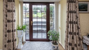 A door with a glass panel, flanked by curtains with a leaf pattern, leading to an outdoor area with a stone pathway and greenery. - Fox's Lair Farmhouse - sleeps 6 guests  in 3 bedrooms (Caernarfon)