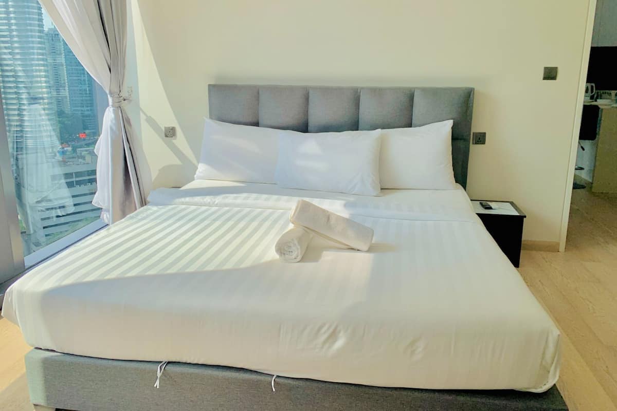 A neatly made bed with white linens, a grey upholstered headboard, and a rolled towel on the bed.
