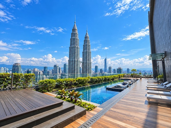 A rooftop pool area with a view of the Petronas Towers, surrounded by greenery and lounge chairs. - STAR KLCC By Comfort Hospitality (Kuala Lumpur)