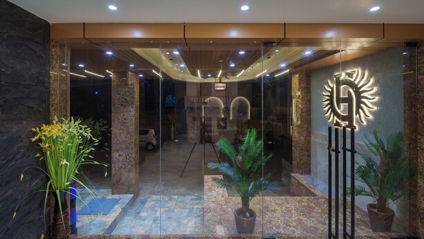 A modern hotel lobby with a glass entrance, potted plants, and a central light fixture. - Hotel Hari Om (Dwarka)